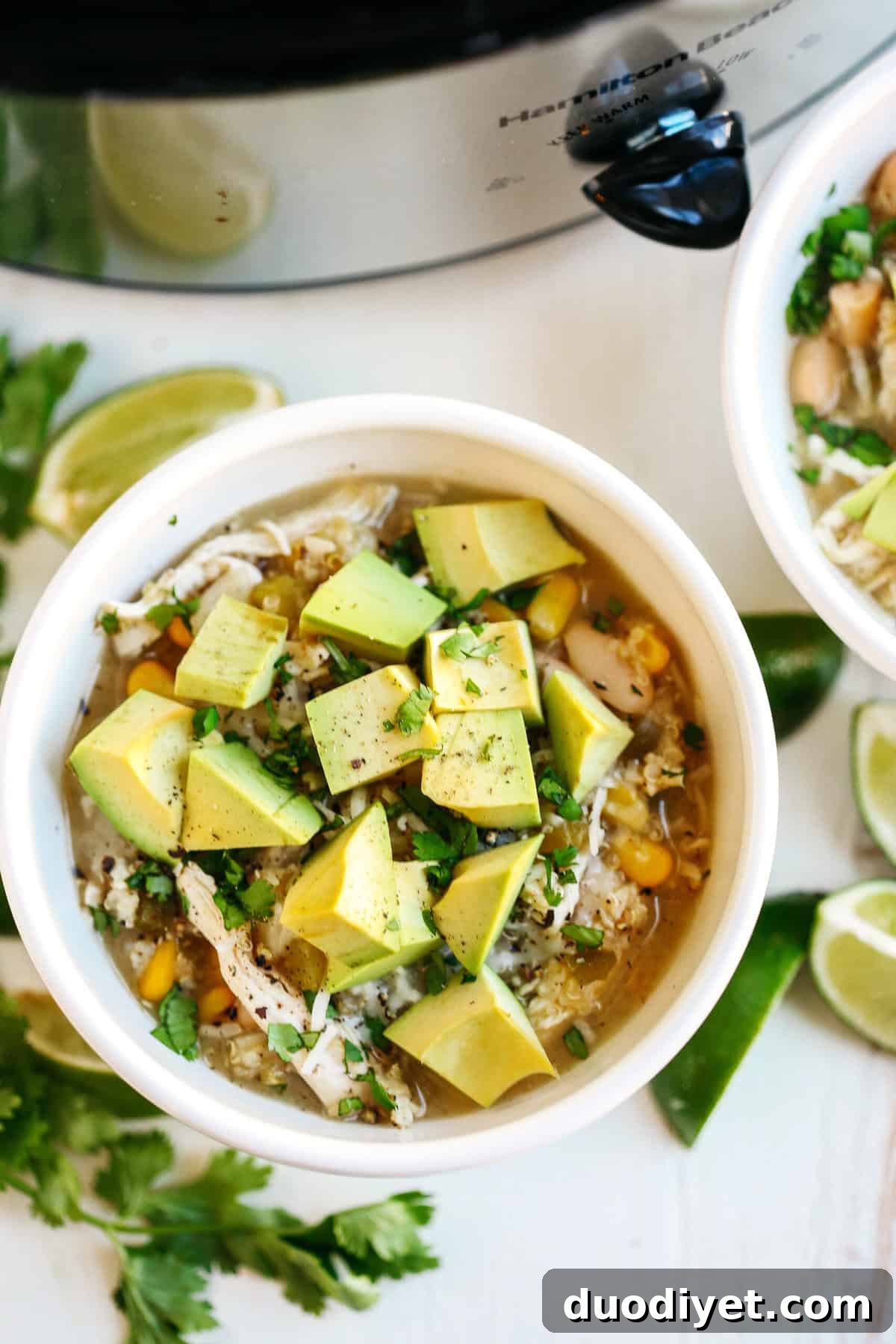 Bowl of white chicken and quinoa chili garnished with avocado and cilantro