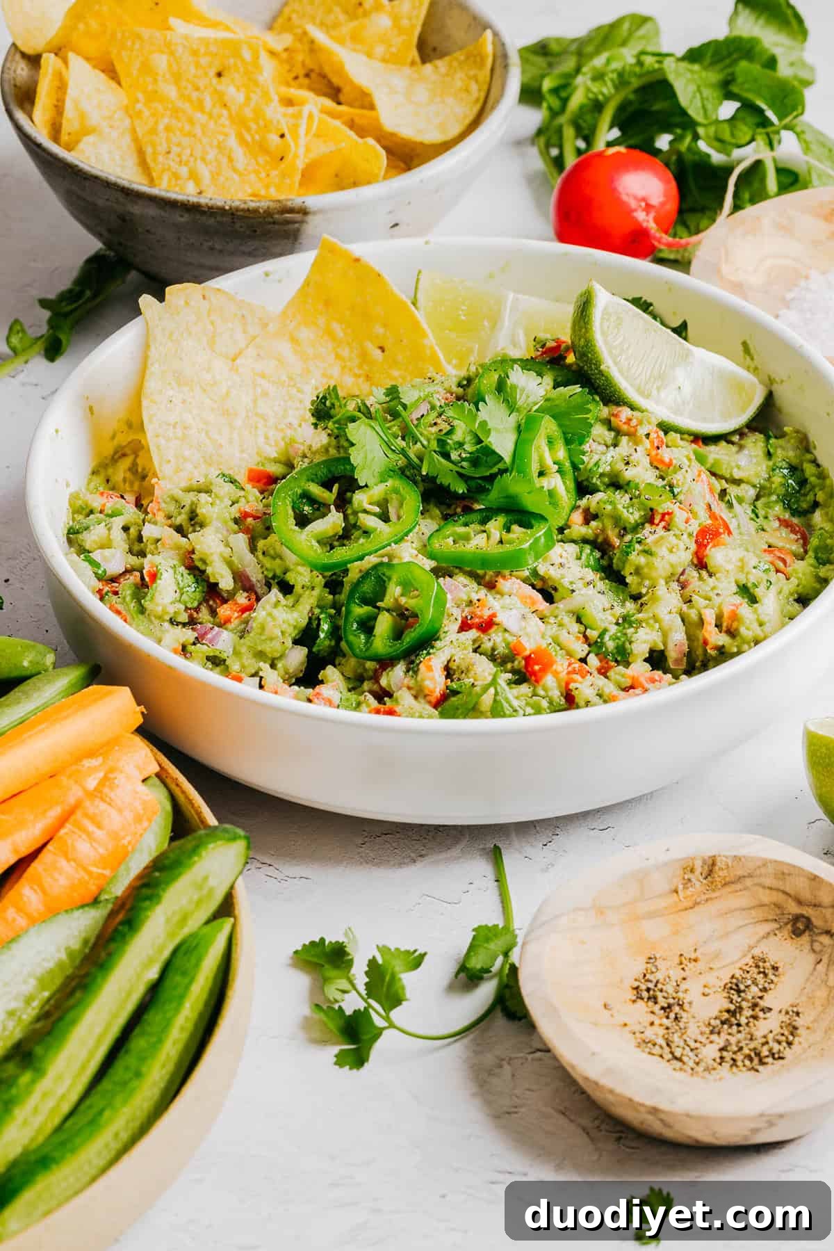 Chunky Guacamole Recipe with Tomato and Onion 7 Guacamole served in a bowl with lime and cilantro.